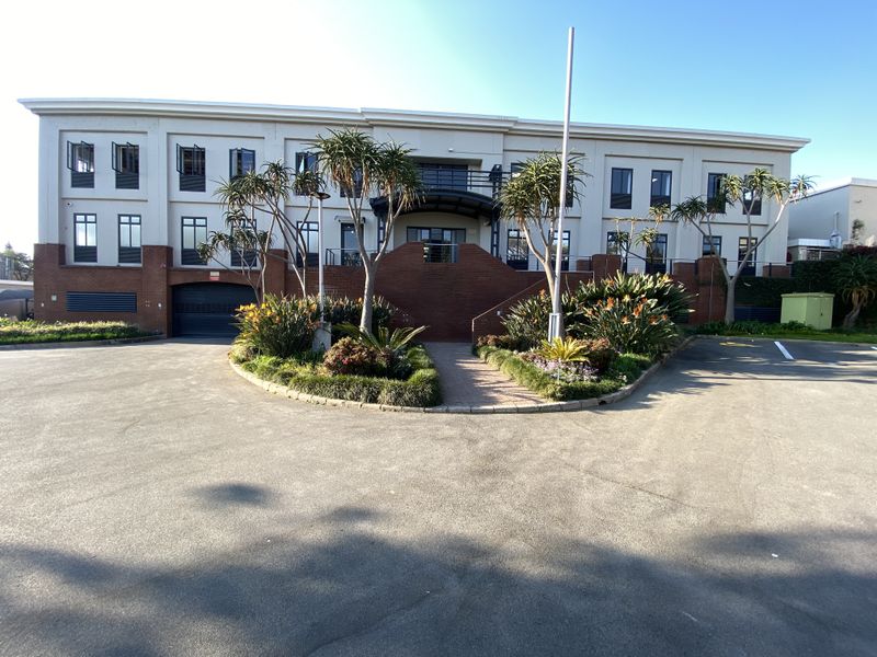 Front elevation of a professional office building featuring a paved driveway, landscaped garden beds, and a central staircase leading to the main entrance.