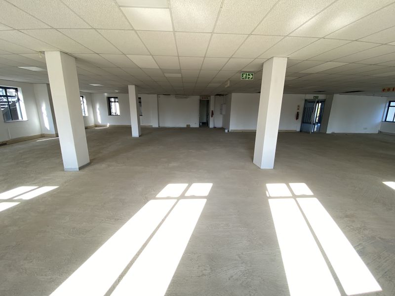 A large, open-plan office space featuring a suspended ceiling, structural columns, and natural light, currently awaiting flooring and final finishes.