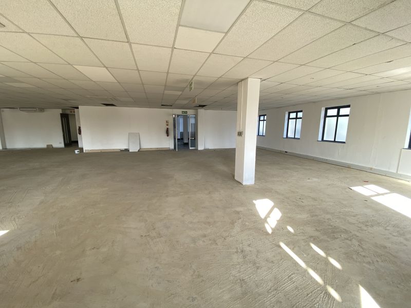 Spacious open-plan office area featuring a suspended ceiling, structural columns, and large windows, currently in a shell condition ready for fit-out.