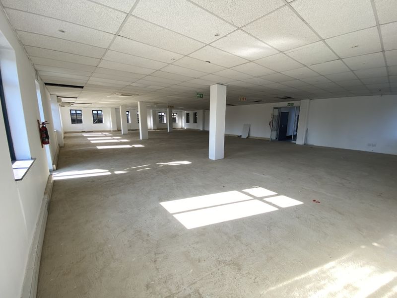 A large, open-plan office space featuring a suspended ceiling, structural columns, and natural light, currently in a shell condition ready for fit-out.