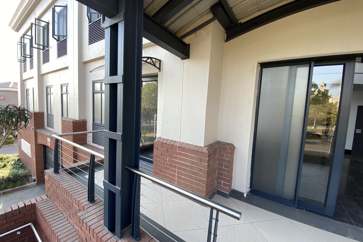 A modern office balcony featuring brick accents, steel structural supports, tiled flooring, and a sliding glass entrance door.