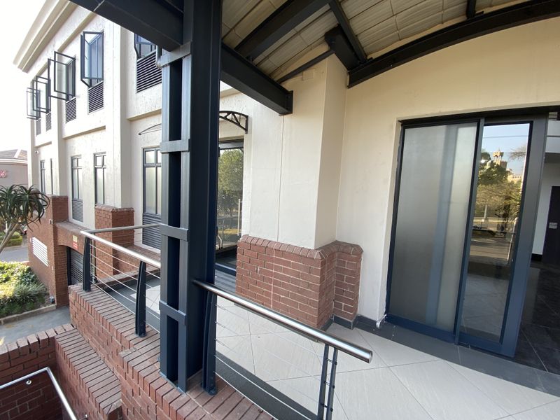 A modern office balcony featuring brick accents, steel structural supports, tiled flooring, and a sliding glass entrance door.
