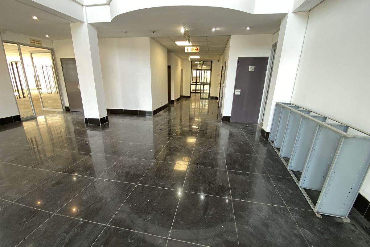 A spacious, well-lit office hallway featuring polished dark granite flooring, structural columns, and clean white walls, providing a professional and modern circulation area.
