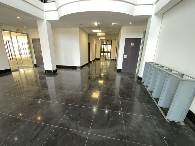 A spacious, well-lit office hallway featuring polished dark granite flooring, structural columns, and clean white walls, providing a professional and modern circulation area.