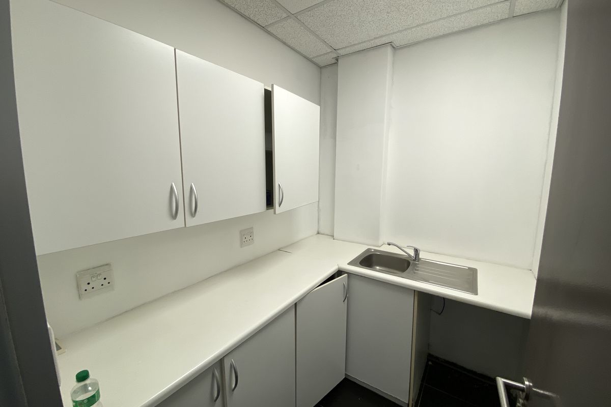 A compact office kitchenette featuring white built-in cabinetry, a stainless steel sink, and a laminate countertop with a drop ceiling.
