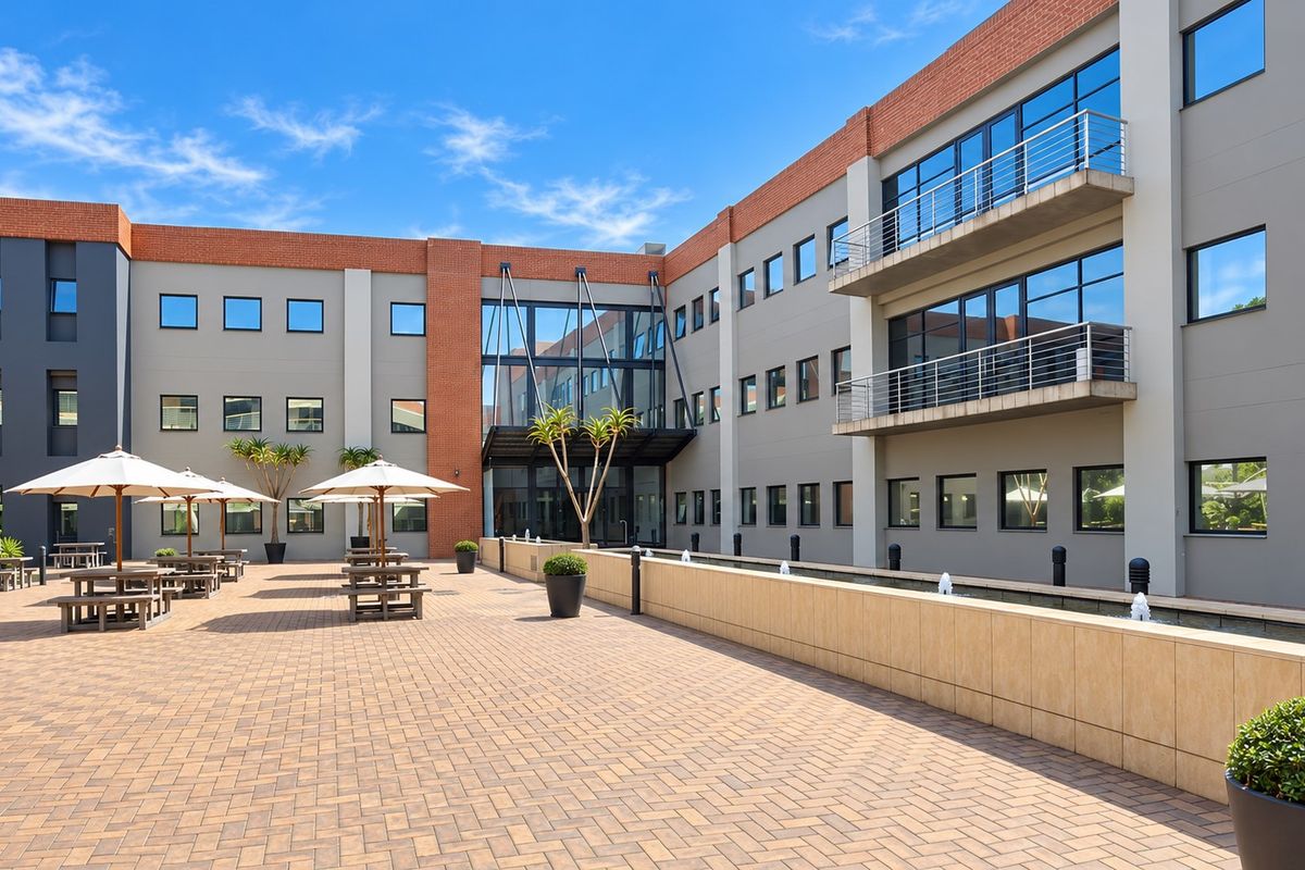 A modern office building exterior featuring a paved courtyard, a central water feature, and multi-level balconies with glass and brick architectural details.