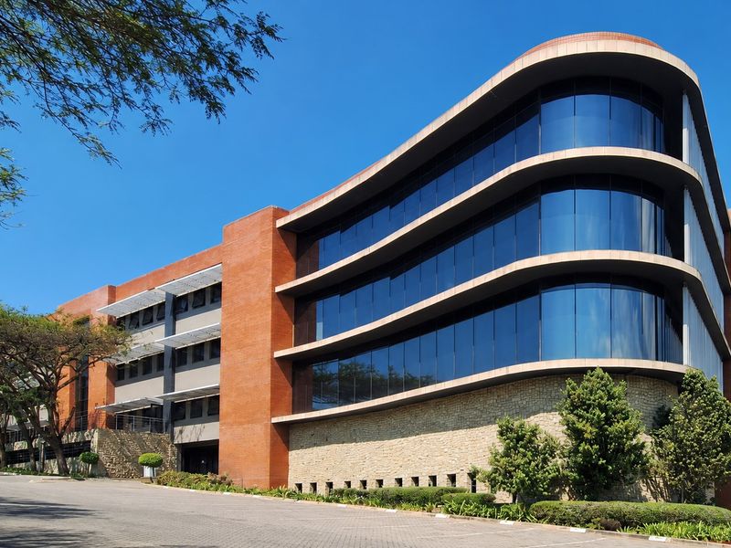 Modern multi-story office building featuring a striking curved glass facade, brick and stone exterior finishes, and integrated sun louvres.