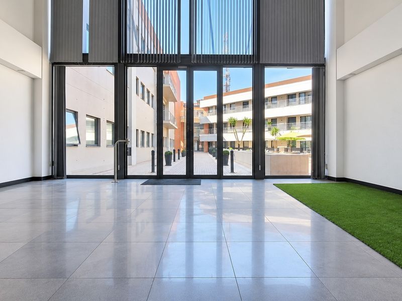 Spacious, modern office entrance hall featuring high ceilings, large glass sliding doors, and polished tiled flooring with an integrated artificial grass feature.