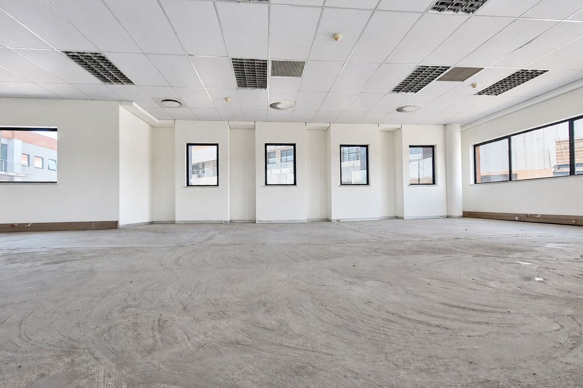 A spacious, open-plan office area featuring a suspended ceiling with recessed lighting, air conditioning vents, and large windows providing ample natural light.