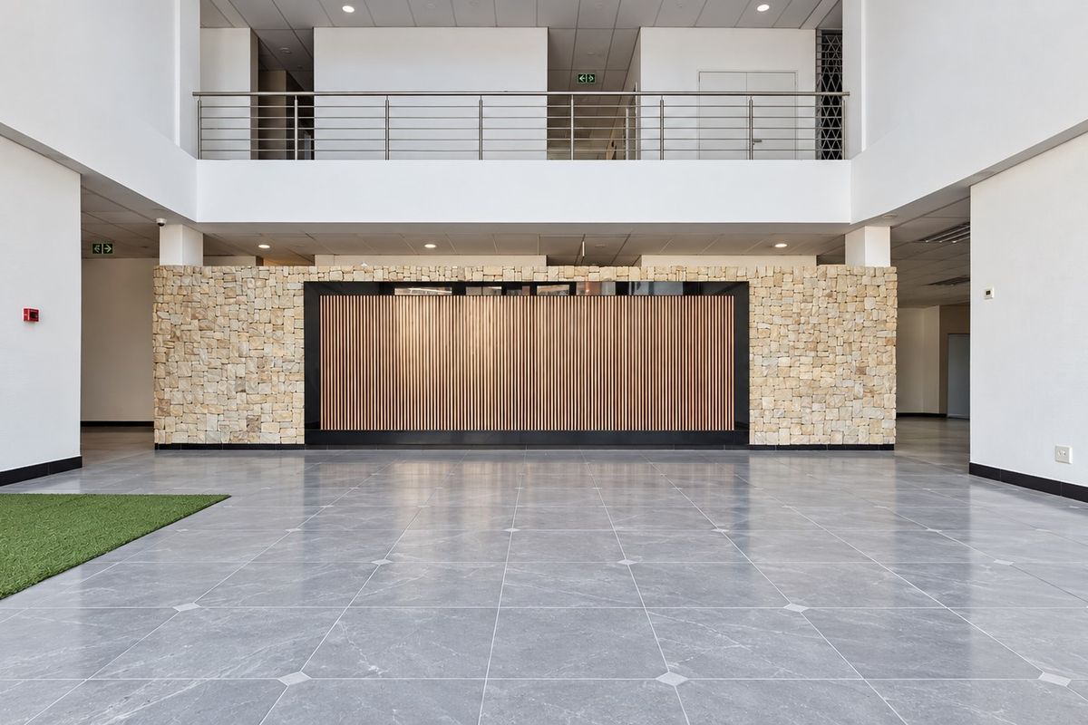 Spacious modern office lobby featuring a double-volume ceiling, stone and timber feature wall, and polished tiled flooring with a mezzanine level overlook.