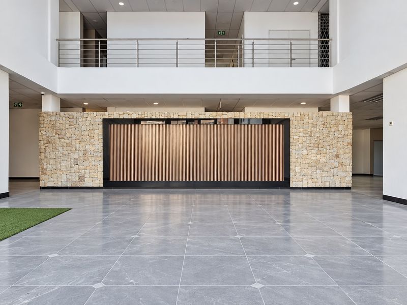 Spacious modern office lobby featuring a double-volume ceiling, stone and timber feature wall, and polished tiled flooring with a mezzanine level overlook.