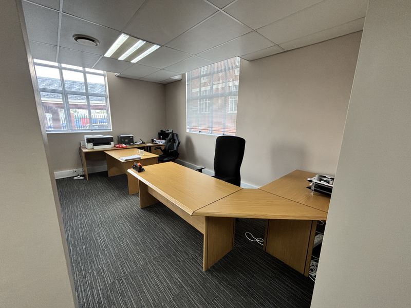 A functional office space featuring a suspended ceiling, recessed lighting, carpeted flooring, and large windows providing natural light.