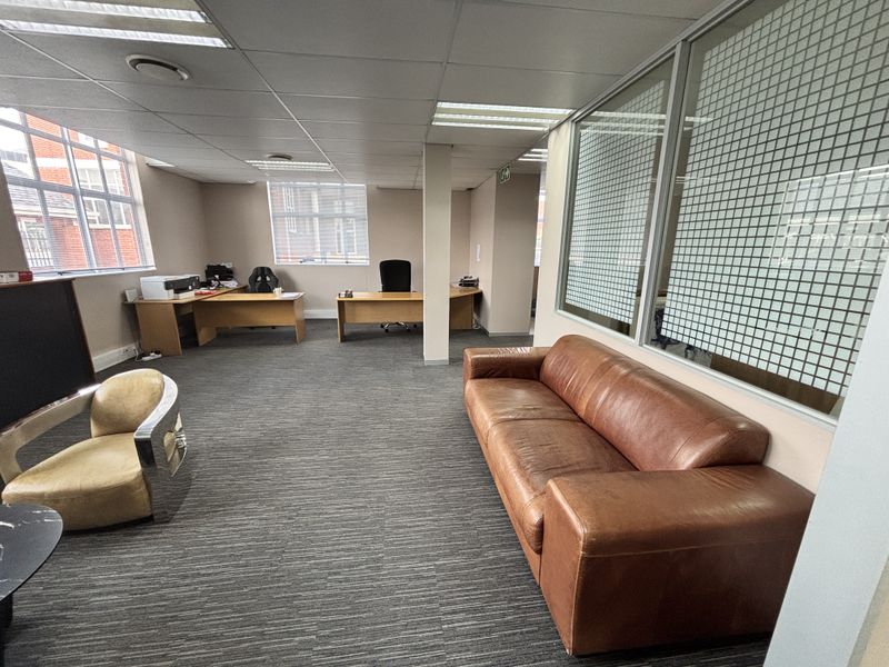 A spacious office area featuring suspended ceilings, recessed lighting, carpeted floors, and glass partitioning, providing a functional workspace with natural light.