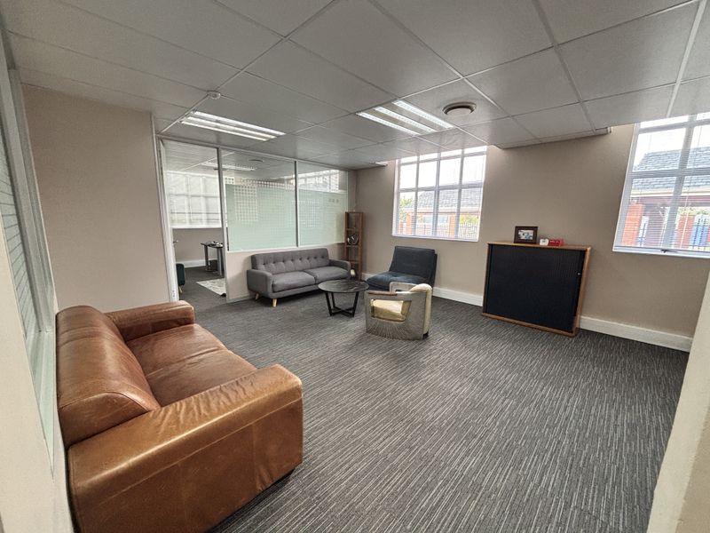 A spacious office area featuring a suspended ceiling, large windows for natural light, and a glass partition wall separating the workspace.