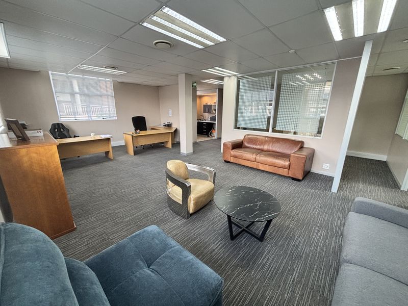 Spacious open-plan office area featuring a suspended ceiling, recessed lighting, carpeted flooring, and a glass partition wall separating the workspace.