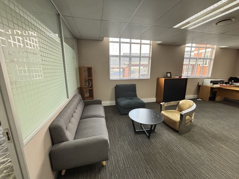 A functional office space featuring a glass partition wall, suspended ceiling with recessed lighting, and carpeted flooring, providing a professional work environment.
