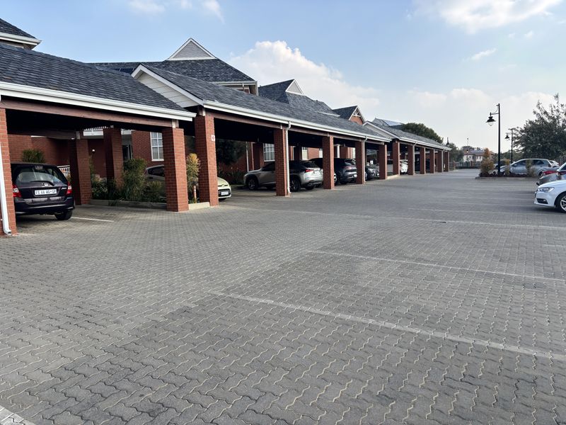 A well-maintained office complex featuring extensive covered parking bays with brick pillars and paved driveway access.