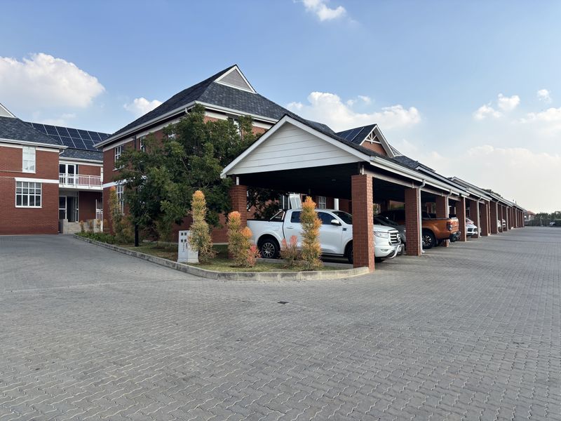 A well-maintained office complex featuring a red brick facade, covered parking bays, and solar panels installed on the pitched roof.