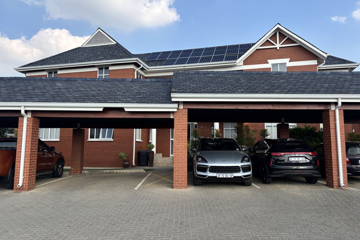Front view of a professional office building featuring a red brick facade, slate roof tiles, integrated solar panels, and covered parking bays.