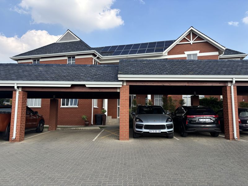 Front view of a professional office building featuring a red brick facade, slate roof tiles, integrated solar panels, and covered parking bays.