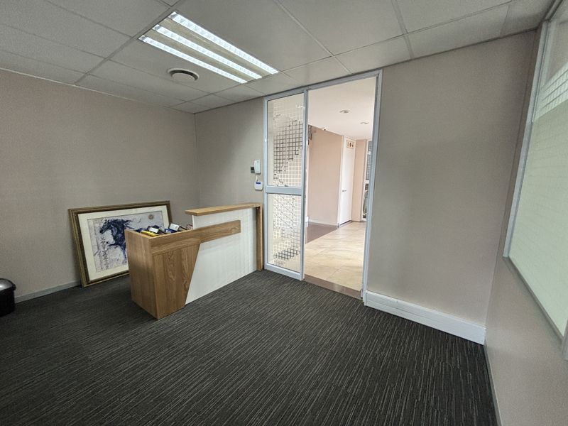 A professional office reception area featuring a built-in desk, glass partition door, suspended ceiling with recessed lighting, and carpeted flooring.