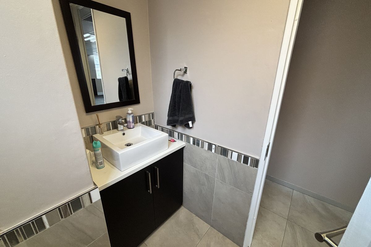 A compact office bathroom featuring a modern vessel sink, dark vanity cabinet, and neutral wall and floor tiling.