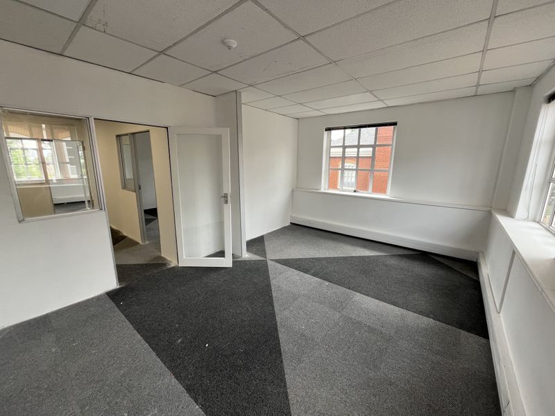 An empty office space featuring a suspended ceiling, patterned carpet tiles, and internal glass partitioning, providing a functional and bright work environment.