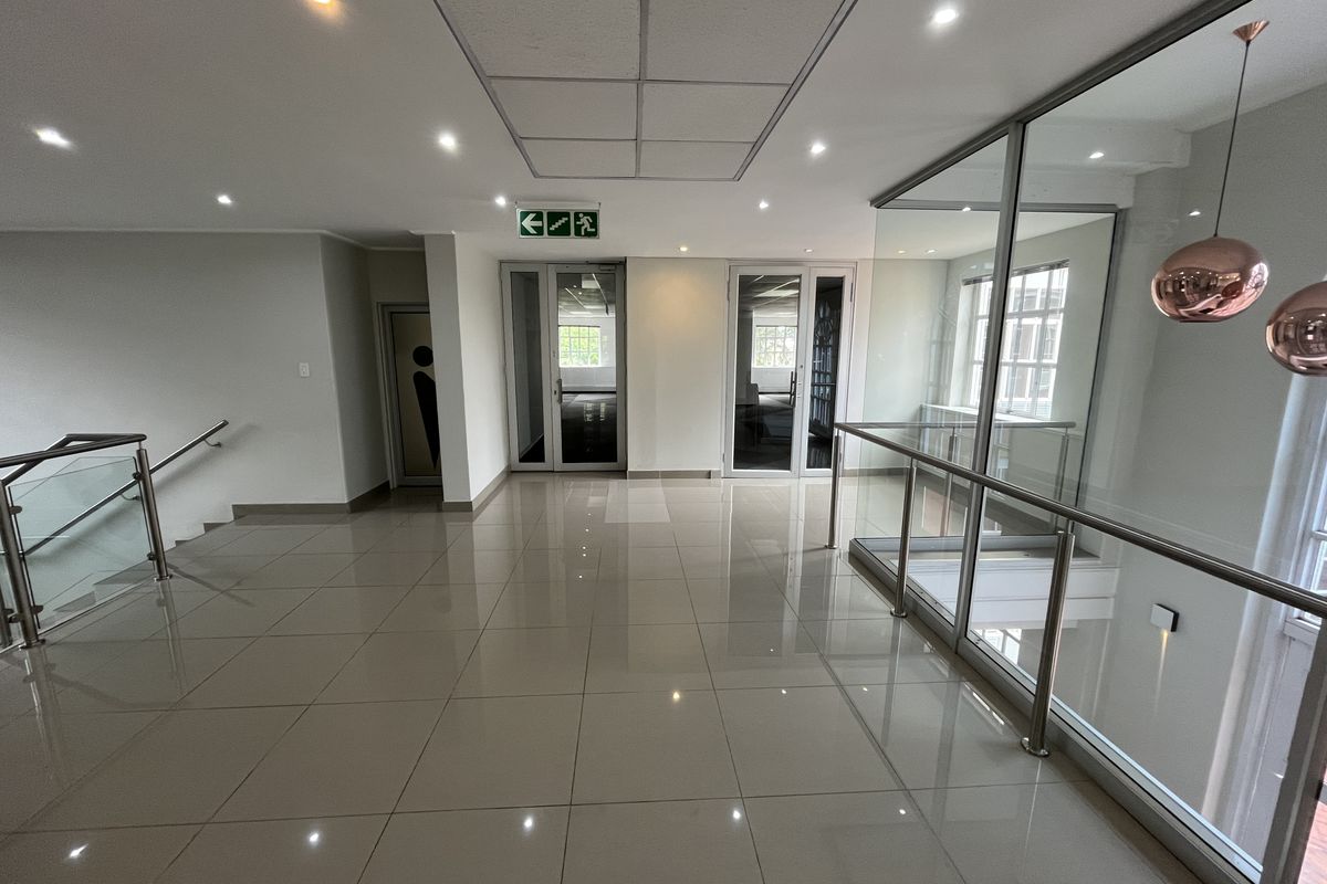 A modern, well-lit office hallway featuring polished ceramic floor tiles, glass balustrades, and clean architectural finishes leading to multiple office entry points.