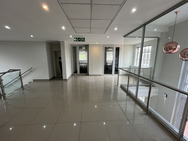 A modern, well-lit office hallway featuring polished ceramic floor tiles, glass balustrades, and clean architectural finishes leading to multiple office entry points.