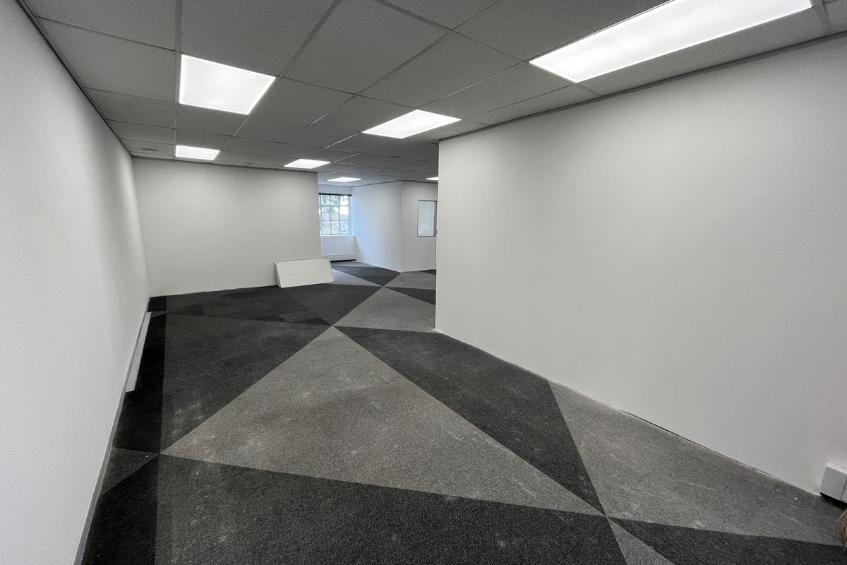 A spacious, vacant office area featuring a suspended ceiling with recessed lighting and modern geometric patterned carpet tiles.