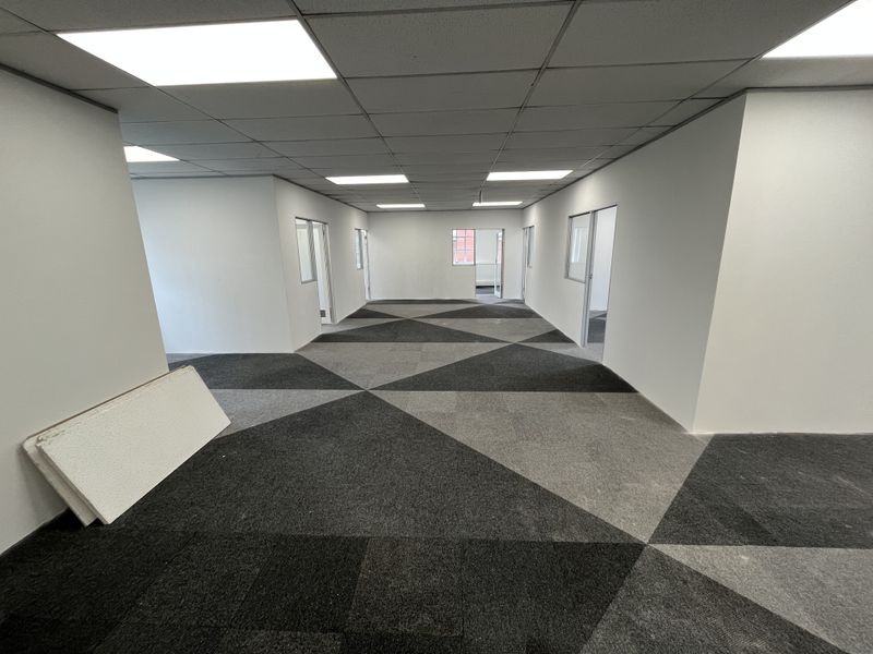 An open-plan office space featuring a geometric patterned carpet, suspended ceiling with recessed lighting, and multiple internal glass-partitioned doorways.