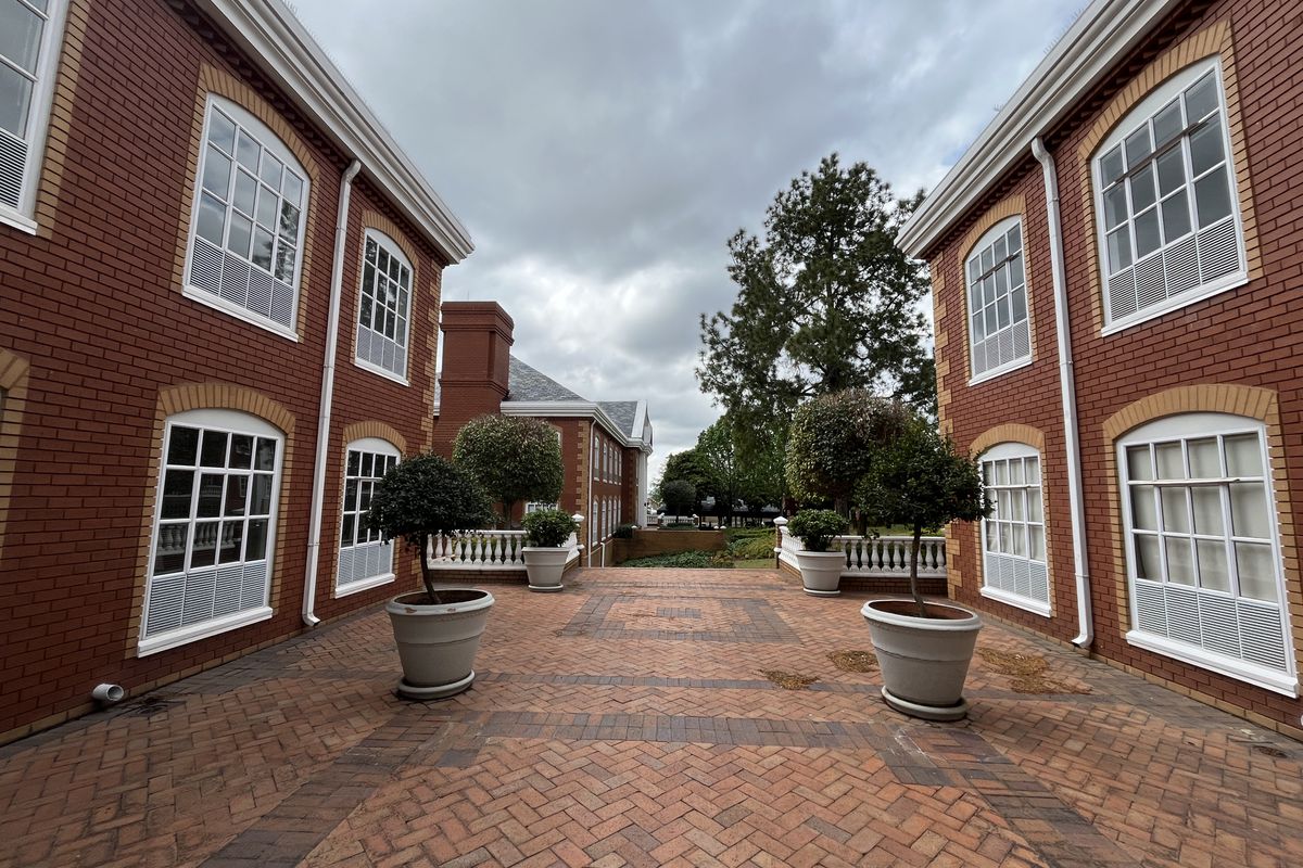 A well-maintained courtyard area featuring classic red brick architecture, herringbone paving, and decorative balustrades between two office building wings.