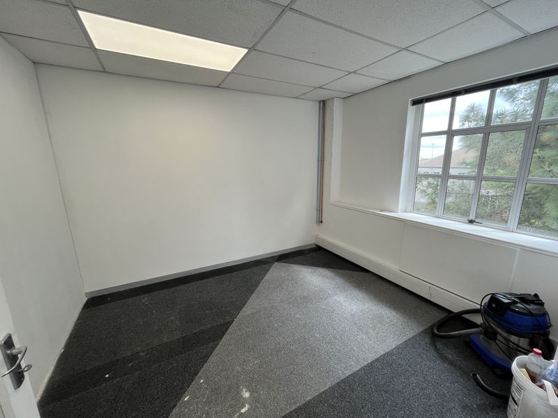 A vacant office space featuring a suspended ceiling, recessed lighting, and large multi-pane windows, providing a functional workspace environment.