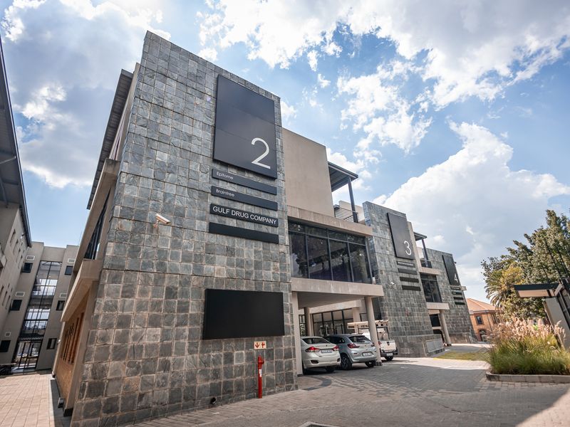 Modern multi-level office building featuring stone cladding, large glass windows, and a paved driveway entrance.