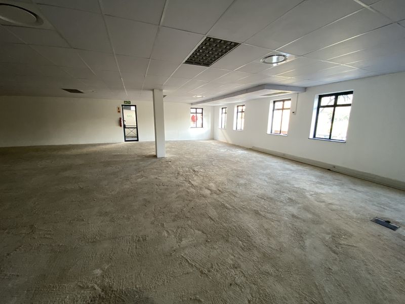 A large, open-plan office space featuring a suspended ceiling, structural column, and multiple windows, currently awaiting flooring installation and final finishes.