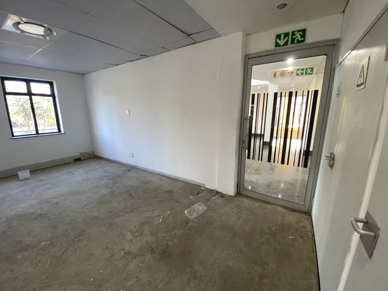 An empty office space featuring a suspended ceiling, aluminium window, and glass door, currently requiring flooring installation and wall finishing.