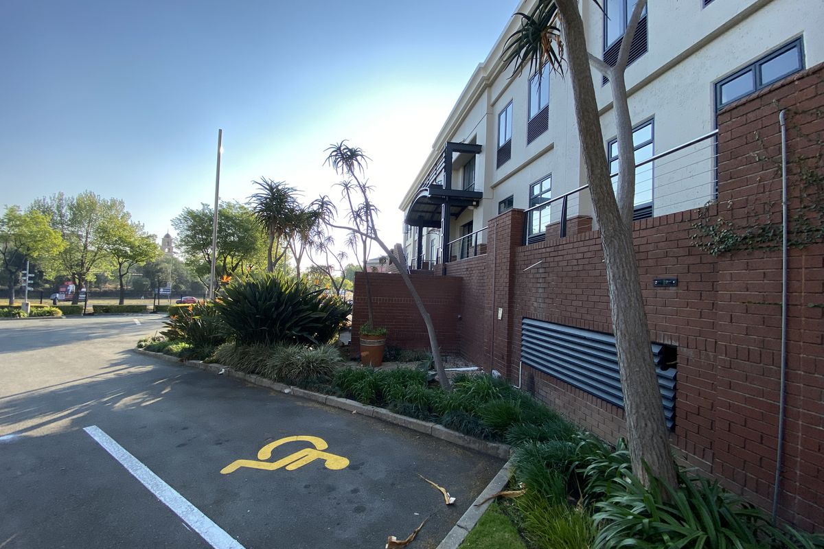 Exterior view of the office building facade featuring a brick retaining wall, metal ventilation louvres, and a designated disabled parking bay.
