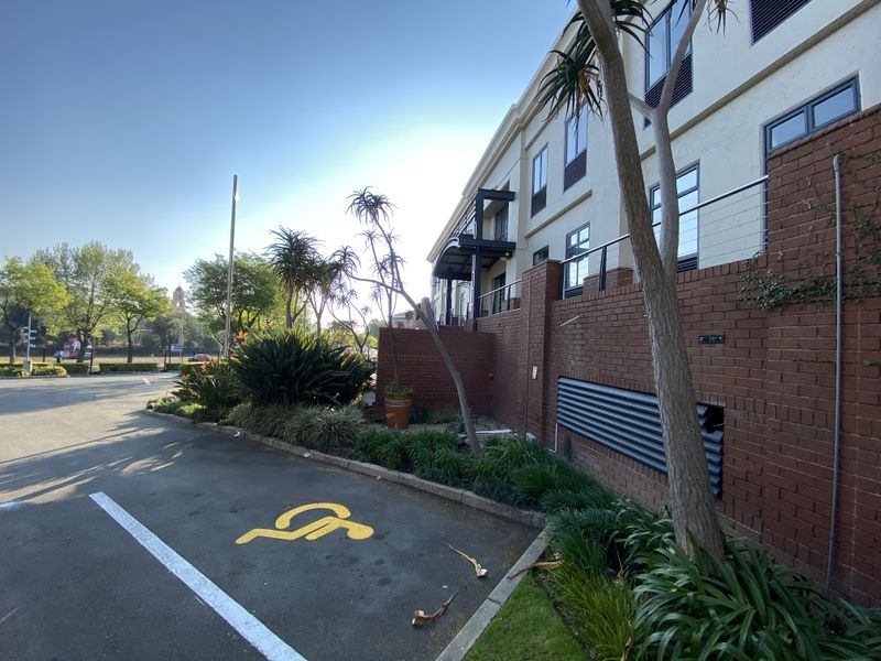 Exterior view of the office building facade featuring a brick retaining wall, metal ventilation louvres, and a designated disabled parking bay.
