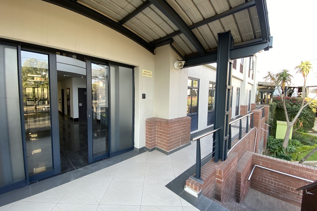A well-maintained exterior walkway featuring sliding glass office access, steel structural supports, brick accents, and a staircase leading to the lower level.