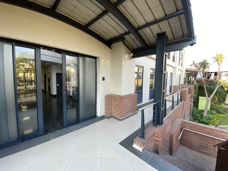 A well-maintained exterior walkway featuring sliding glass office access, steel structural supports, brick accents, and a staircase leading to the lower level.