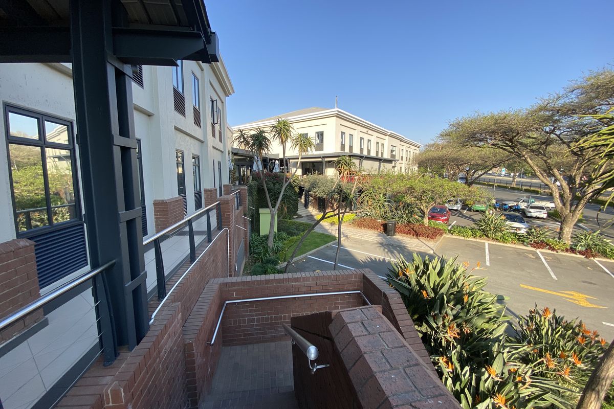 Exterior view of an office complex featuring a brick staircase, landscaped garden areas, and an adjacent paved parking lot.