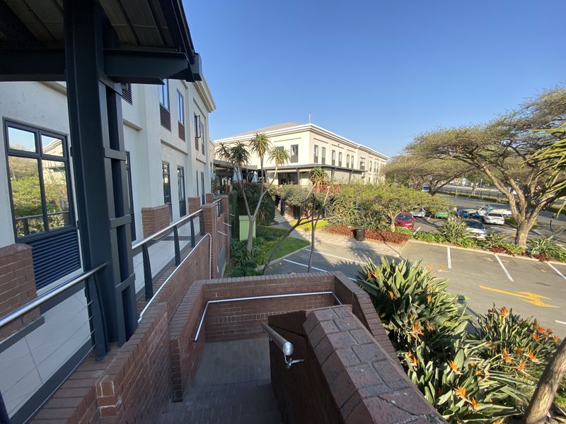 Exterior view of an office complex featuring a brick staircase, landscaped garden areas, and an adjacent paved parking lot.