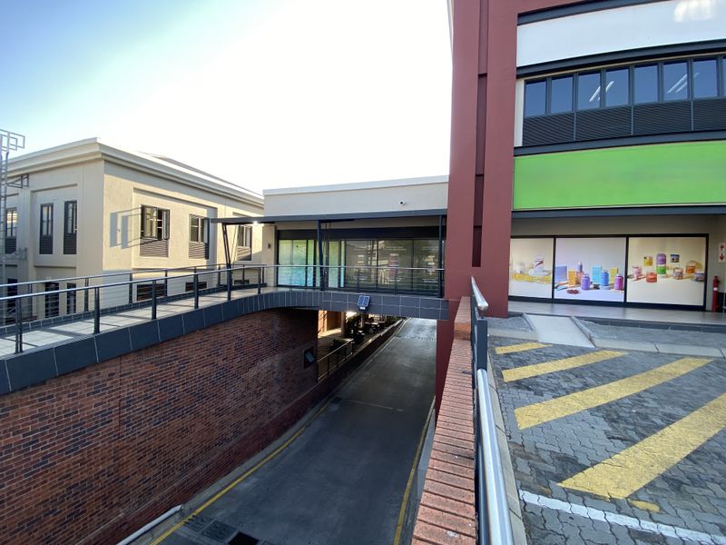 Exterior view of a commercial retail property featuring a pedestrian bridge connecting buildings over a driveway with modern brick and glass architectural elements.