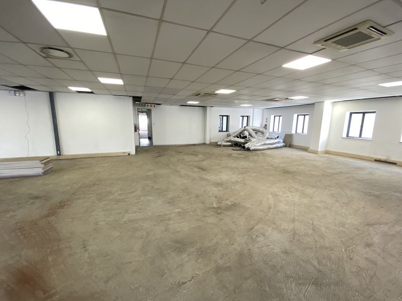A large, open-plan retail or office space featuring a suspended ceiling with recessed lighting, ducted air conditioning, and unfinished concrete flooring.