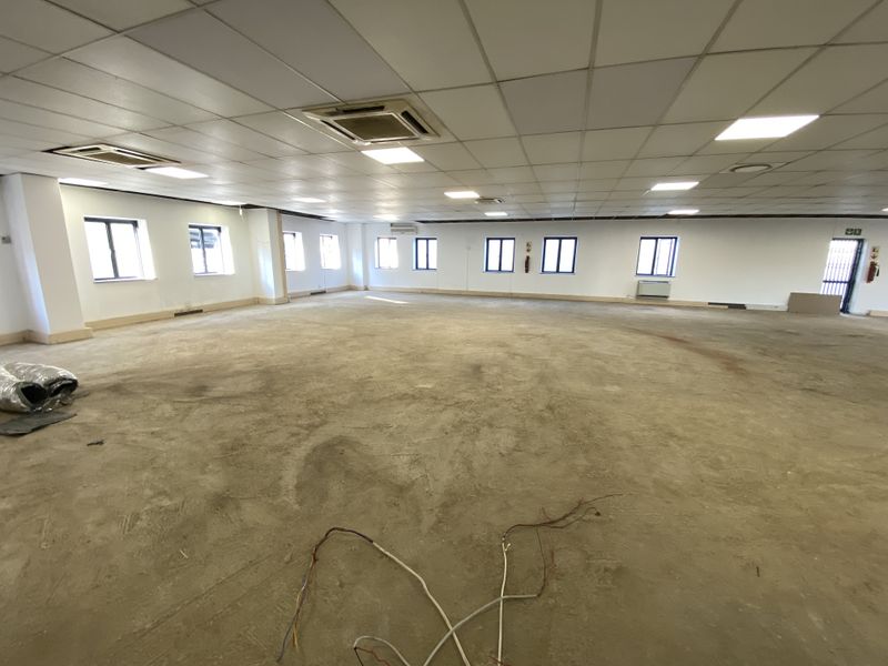 A large, open-plan retail or office space featuring a suspended ceiling, recessed lighting, cassette air conditioning, and unfinished flooring ready for final finishes.