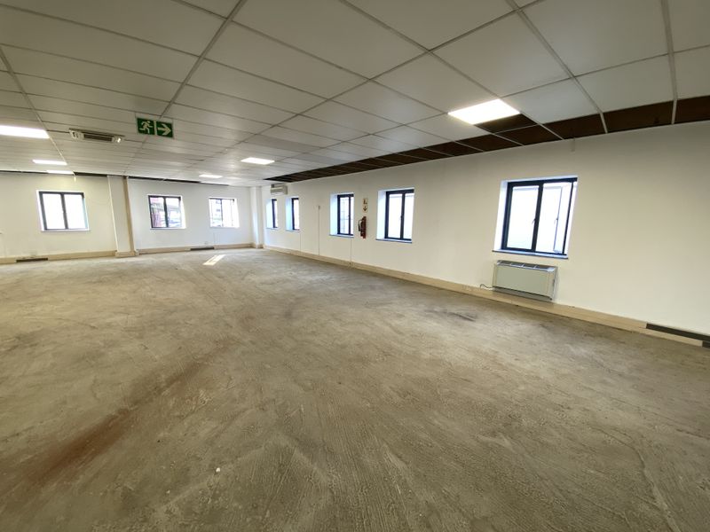 A large, vacant open-plan retail space featuring a suspended ceiling, recessed lighting, air conditioning, and multiple windows with aluminium frames.
