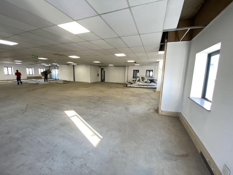 A large, open-plan commercial retail space featuring a suspended ceiling, recessed lighting, and concrete flooring, currently undergoing renovation or fit-out.