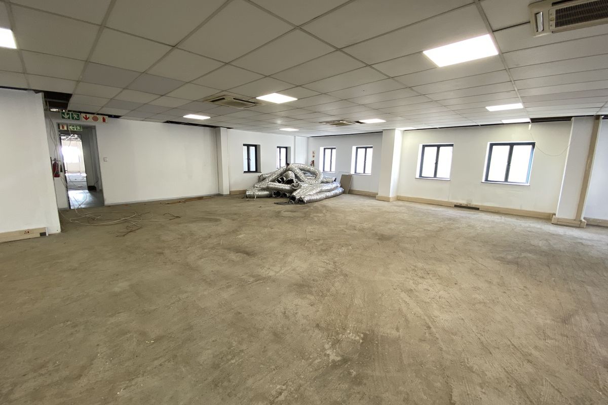 A large, open-plan retail or office space featuring a suspended ceiling, recessed lighting, and unfinished concrete flooring, ready for custom fit-out.