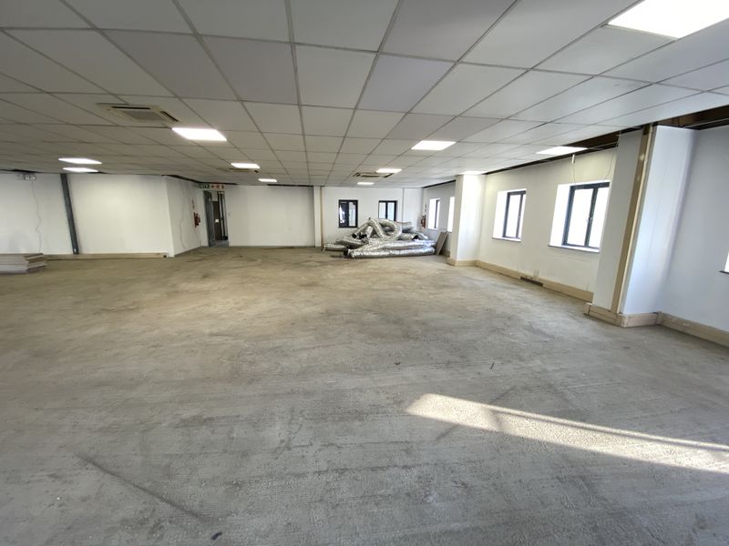 Spacious open-plan retail or office area featuring a suspended ceiling, recessed lighting, ducted air conditioning, and large windows providing natural light.