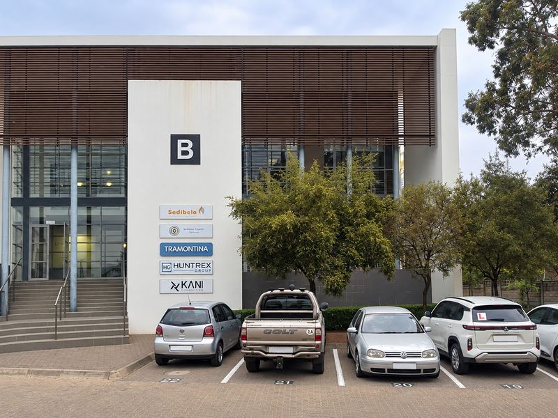 Front elevation of a modern commercial office building featuring a glass facade, louvred sun screening, and dedicated paved parking bays.